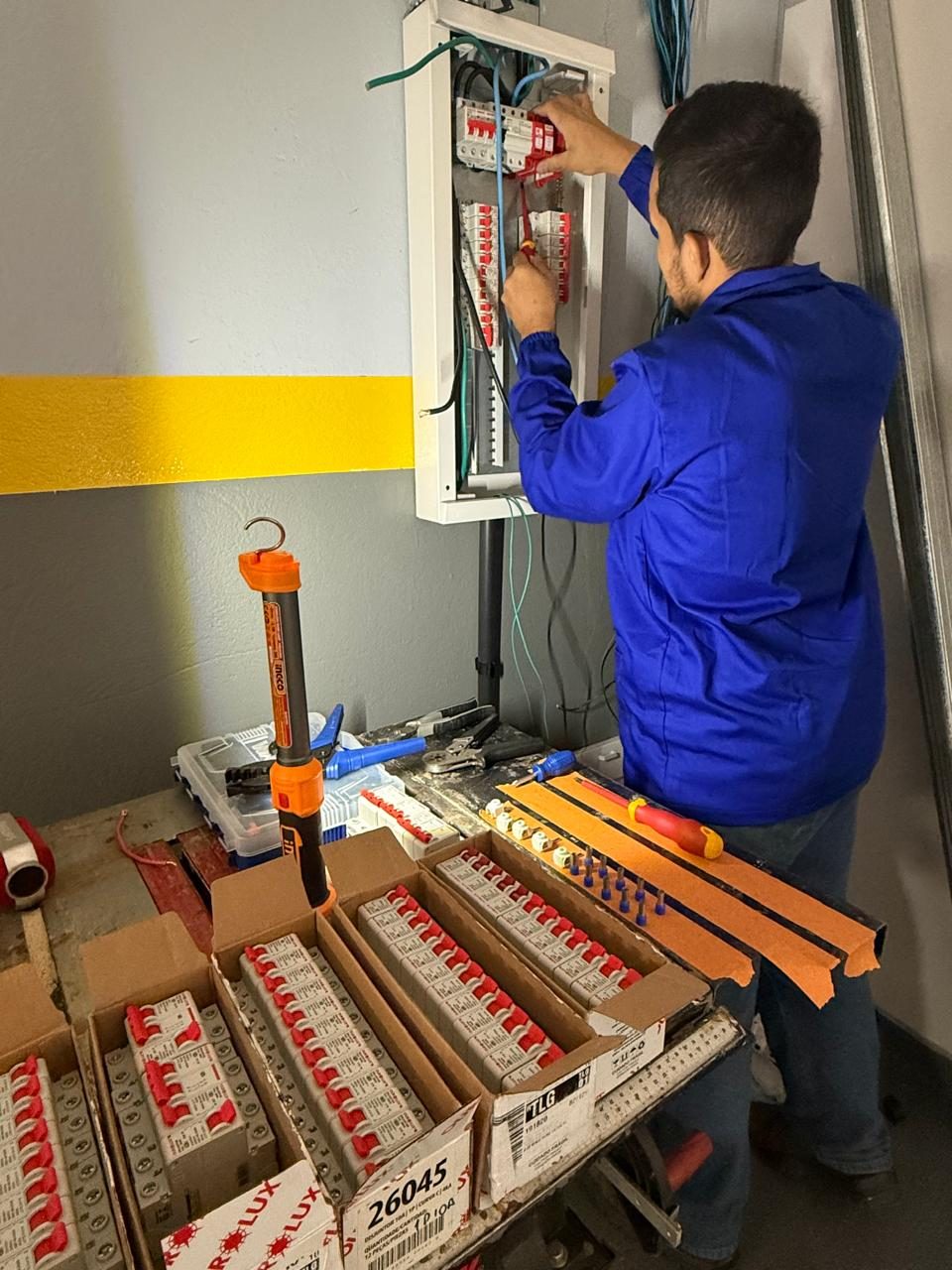 Eletricista montando quadro de distribuição com caixas de disjuntores ao lado